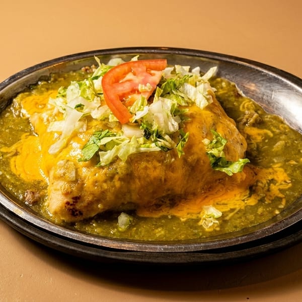 Smothered burrito with green chile sauce, melted cheese, lettuce, and tomato in a metal dish.